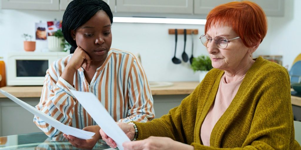 Personal assistant working with a disabled person. They are sitting together at a kitchen table looking at paperwork.