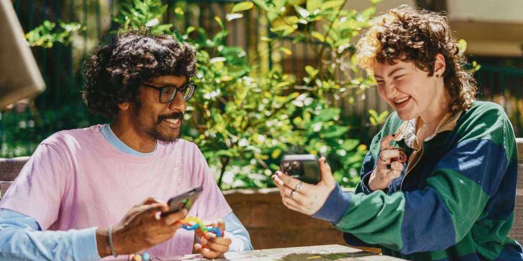 Two people at a table looking at mobile phones and laughing.