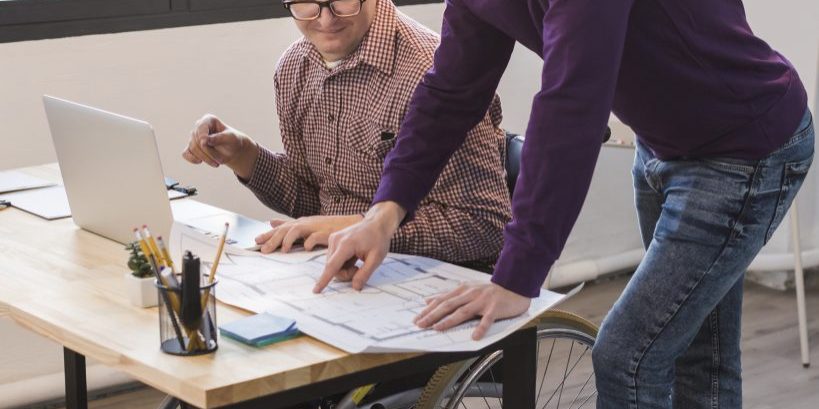 Manager working together with disabled man on what look like architects drawings.